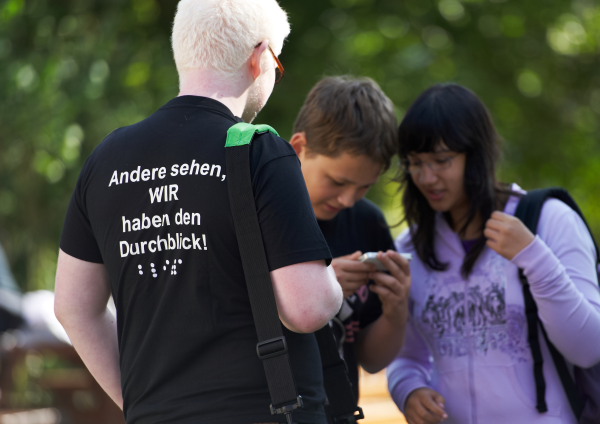 Drei Schüler schauen auf ein Handy. Einer trägt ein T-Shrit mit der Aufschrift "Andere sehen, WIR haben den Durchblick". (Foto: blista)