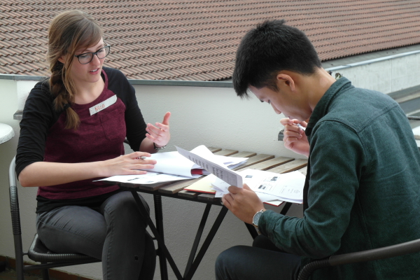 Wir schulen unsere Mentorinnen und Mentoren für ihr Ehrenamt. Das Bild zeigt eine Mentorin und einen Mentor vertieft in Unterlagen auf einem Balkon. (Foto: ArbeiterKind.de)