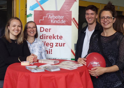 Vier Ehrenamtliche stehen am Infostand und lächeln in die Kamera. Eine Mentorin hält einen Luftballon von ArbeiterKind.de in der Hand. (Foto: ArbeiterKind.de)