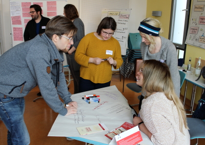 Aufnahme vom vergangenen Gruppenkoordinationstreffen in Lübeck. Vier Menschen diskutieren. Sie bearbeiten nebenbei ein Flipchartpapier. (Foto: ArbeiterKind.de)