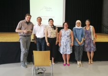 Gruppenfoto von unserem Schulvortrag an der Käthe-Kollwitz-Schule. Im Hintergrund läuft unsere Präsenation und vor der Bühne lächeln alle in die Kamera. (Foto: ArbeiterKind.de)